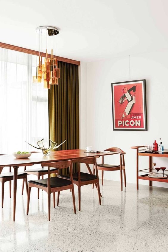 An elegant and refined mid century modern dining room with a long table and black chairs, a bar cart, green curtains, an amber glass chandelier and a print