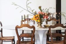 an elegant dining room with a large oval dining table, vintage stained chairs, an arched mirror in a black frame and blooms