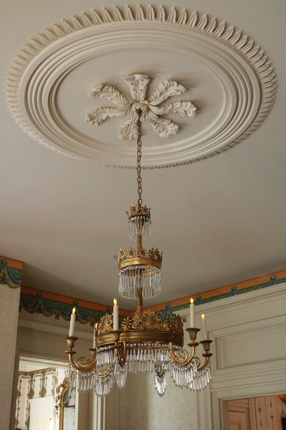 An oversized refined off white ceiling medallion that matches the color of the ceiling and a whimsical crystal and gold chandelier with candles