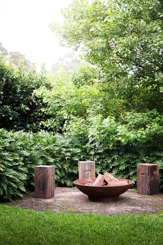 a small outdoor nook with a fire bowl and tree stumps around it is a lovely idea to spend your time in, it's relaxed and cool