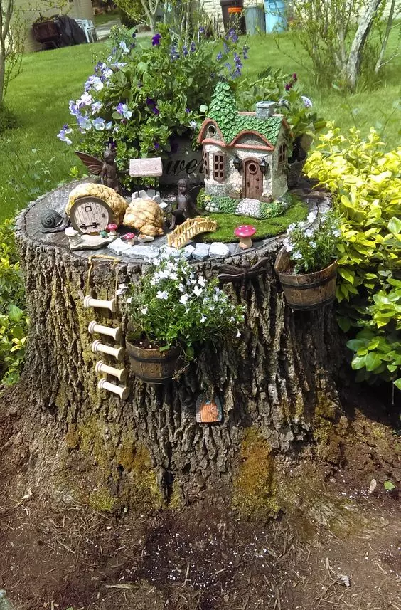 a lovely and cute garden decoration made of a tree stump, a little elf house, some blooms and greenery and more tiny figurines