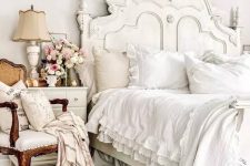 a sophisticated neutral French chic bedroom with a refined bed and bedding, a dresser, a chic creamy chair, a lovely lamp and some blooms