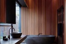 02 a contemporary bathroom with wood slat walls, a black lit up ceiling, a black bathtub on a stone platform, a black sink and a radiator