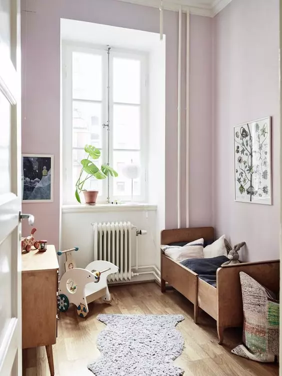 a cute and small kid's space with light pink walls, a stained and a desk, artwork, rugs and a basket for storing toys