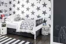 07 a monochromatic Scandinavian kid’s room with a star-printed accent wall, ledges for books, a wihte bed with drawers, a wardrobe with a chalkboard and a striped rug