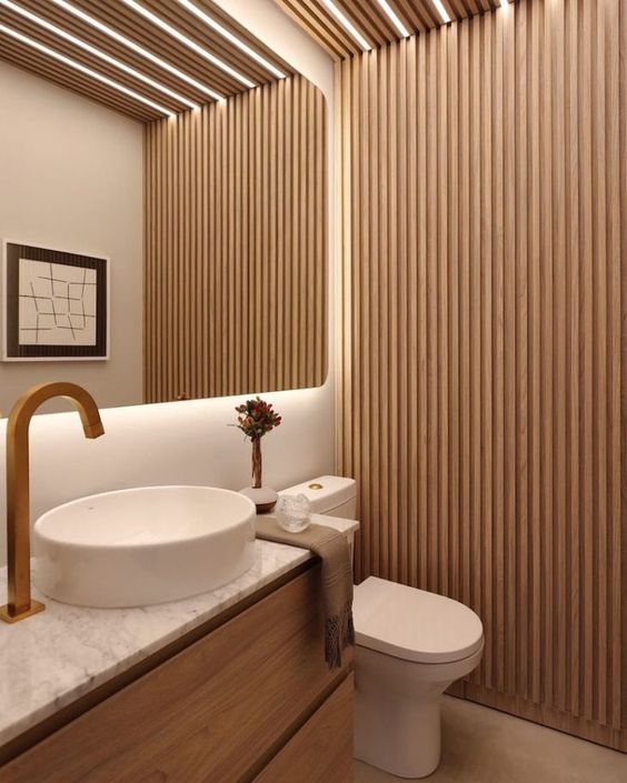 A contemporary neutral bathroom with a wood slat accent wall, a floating vanity, a white sink and a toilet and built in lights