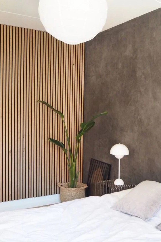 A minimalist bedroom with a concrete wall and a wood slat accent wall that hides a built in wardrobe and adds coziness to the space