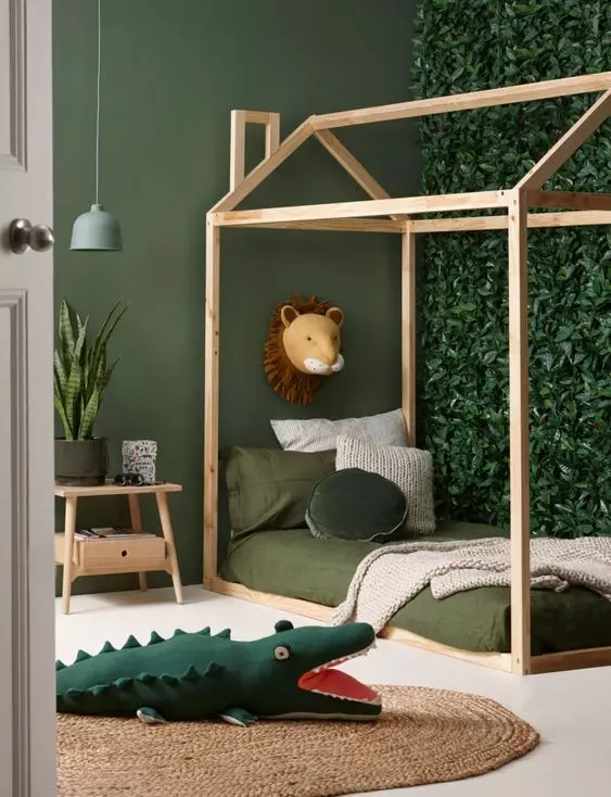 A small jungle kids' room with a faux greenery accent wall, a house shaped bed with green bedding, a jute rug and a nightstand with plants