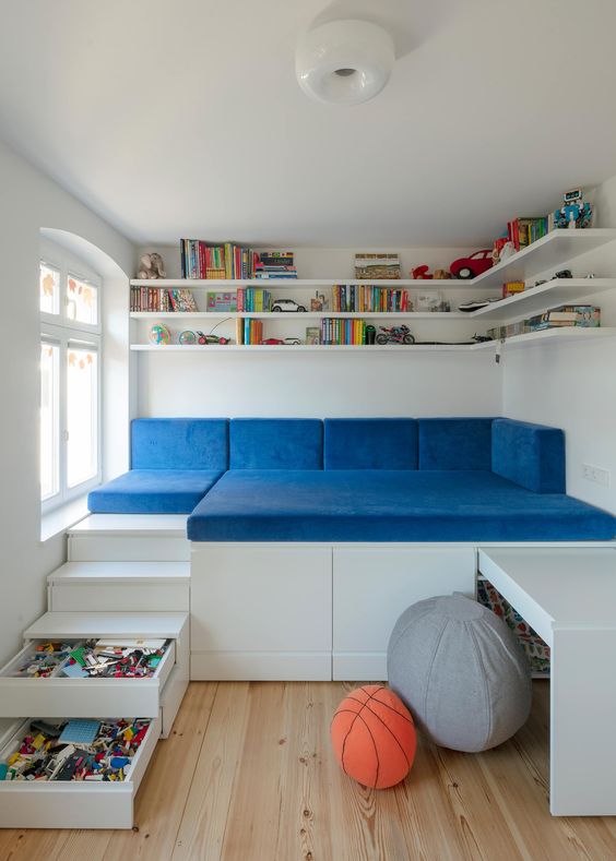 A small kid's space with open shelves, a raised sofa to sleep on, storage drawers and a built in desk and bright touches