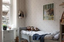 23 a small Scandi kids’ room with printed wallpaper, a grey bed, a white cabinet, open shelves and a wicker chair