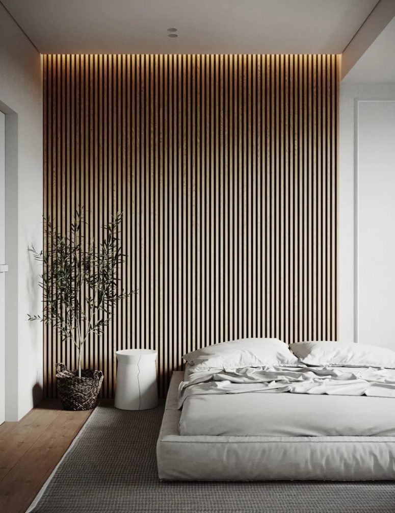a neutral minimalist bedroom with a wood slat accent wall with lights over it, a low soft bed with neutral bedding and a potted tree