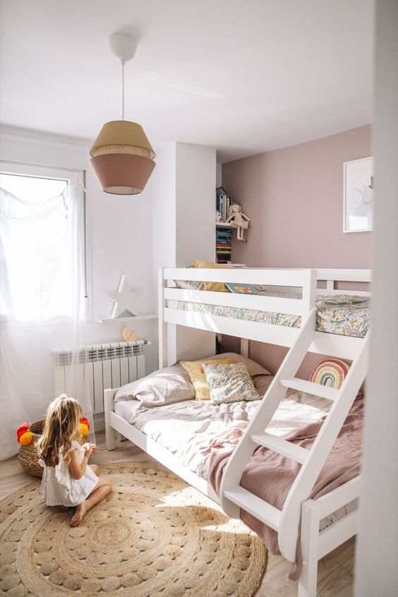 A beautiful mauve kids' bedroom with a bunk bed, a jute rug, a storage unit and open shelves plus a two tone lamp