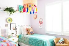 31 a pastel shared kids’ bedroom with lavender walls and a pouf, colorful bedding and art and a lamp with colorful tassels