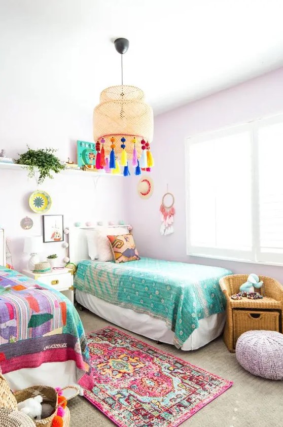 a pastel shared kids' bedroom with lavender walls and a pouf, colorful bedding and art and a lamp with colorful tassels