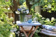 34 a lawn around the tree used as a little dining space, with stained folding furniture, cushions and pillows, hanging candle lanterns and blooms
