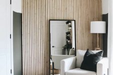38 a neutral mid-century modern living room with color block walls, a wood slat accent wall, a floor mirror, a neutral chair and jute poufs