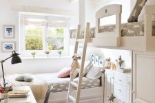 39 a small shared kids’ room with a raised and usual bed, a ladder, printed bedding, a white desk and a black chair