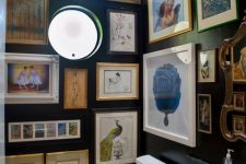 a black powder room with a round window, vintage artwork all over the space, white appliances and lights here and there