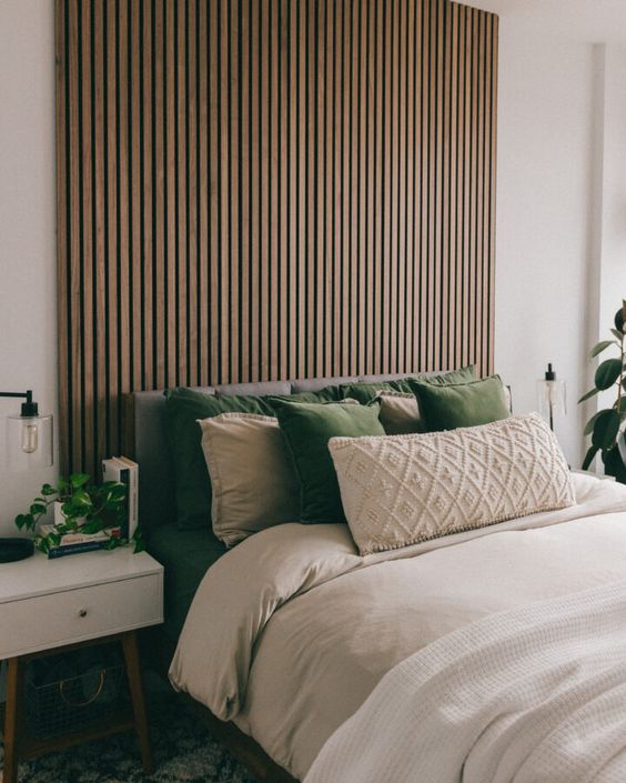 a boho bedroom with a stained wood slat wall, a bed with green and neutral bedding, white nightstands, potted greenery