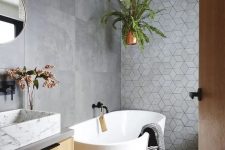 a contemporary bathroom with large scale concrete and geometric tiles, an oval tub, a floating vanity and a white marble sink plus greenery