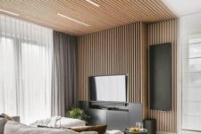 a contemporary living room with a wood slat wall and a ceiling, a TV , a neutral sofa and a pouf plus coffee tables