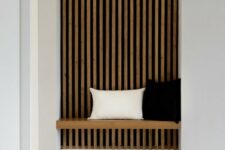 a laconic Japandi entryway with a wood slat accent wall and lights, a built-in daybed and a wooden stool and jute rug
