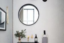 a modern and catchy bathroom with a black floating sink, a round mirror, a black retro sconce and some greenery in a vase