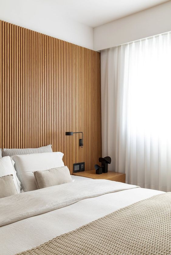 a modern bedroom with a wood slat accent wall, a bed with neutral bedding, a nightstand, black sconces and lamps