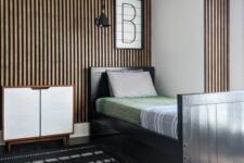 a modern kid’s room with a wood slat accent wall, a black bed with bright bedding, a black and white rug and a dresser