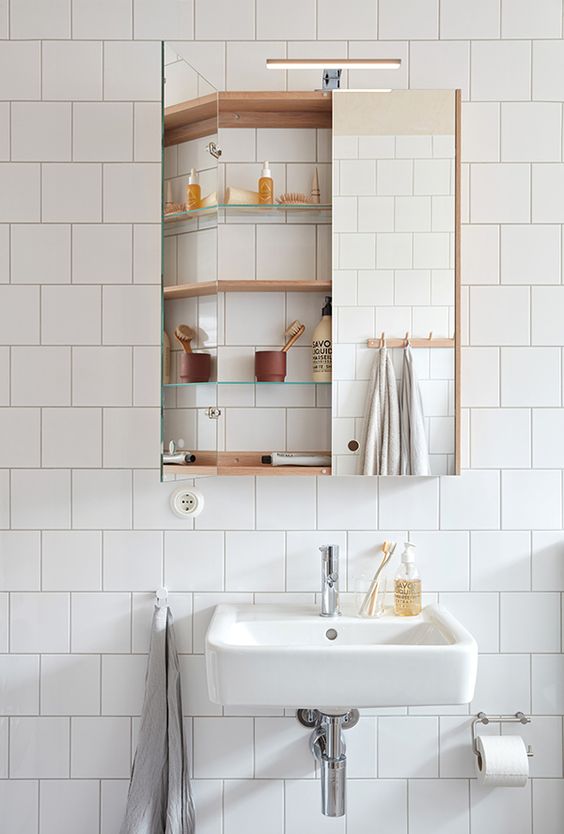 A modern white bathroom with a mirror storage cabinet, a floating sink and some light stained wood is a lovely and airy space