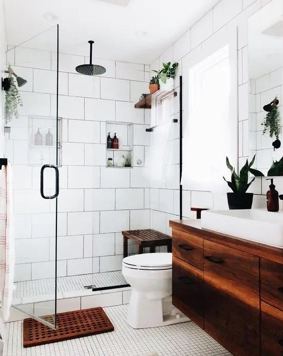a modern white bathroom with various types of tiles, a dark stained floating vanity and a matching mat and bench, potted greenery