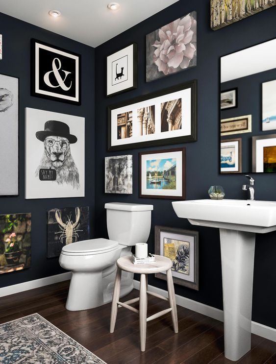 a navy bathroom with a gallery wall that takes all the blank wall space, white appliances and a mirror integrated into this art spot