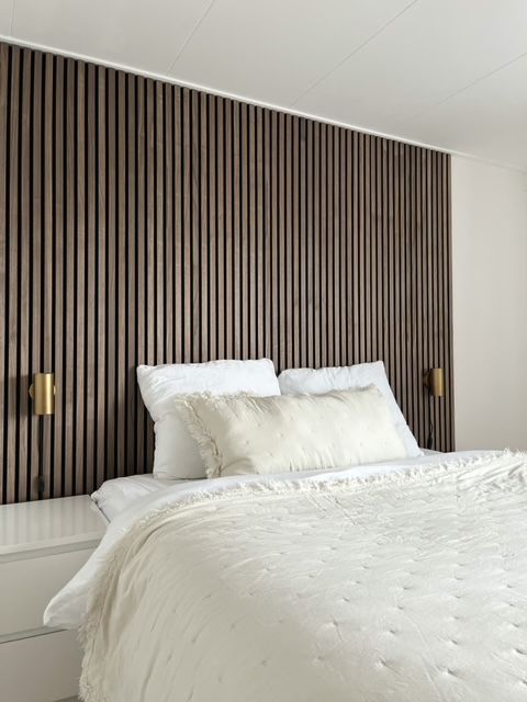 A neutral bedroom with a dark stained wood slat accent wall, white nightstands, a bed with neutral bedding