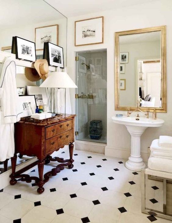 A neutral vintage bathroom with a checked floor, a vintage stained dresser, a free standing sink, a gallery wall and a mirror