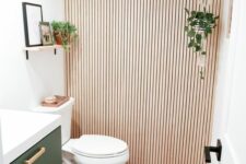 a small and lovely powder room with a wood slat accent wall, a green floating vanity, a shelf, some decor and greenery
