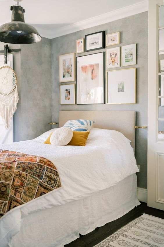 a small boho bedroom with grey limewashed walls, a neutral upholstered bed and neutral bedding, a small yet chic gallery wall and a dream catcher