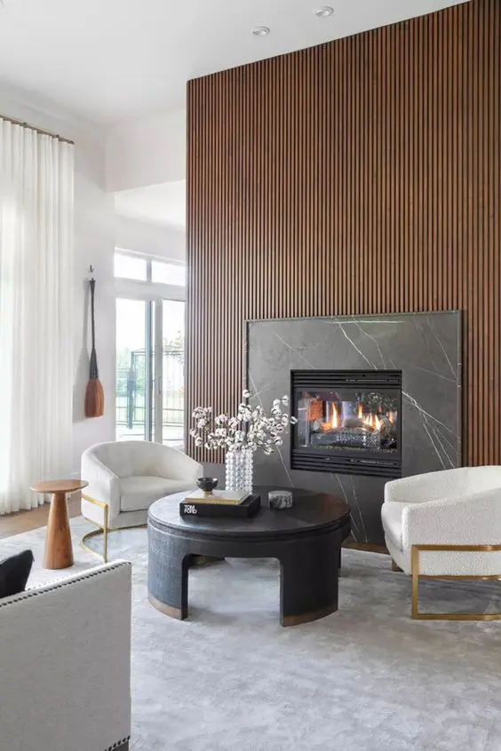 A sophisticated living room with neutral walls, a rich stained wood slat wall with a built in fireplace, white chairs and a round coffee table