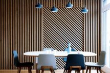 a stylish dining room with a wood slat accent wall, an oval table and navy and white chairs, pendant lamps over the table
