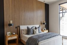 an elegant modern bedroom with a wood slat accent wall, a bed with neutral bedding, stained nightstands, black and gold sconces