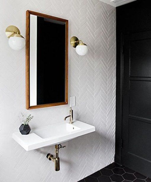 An elegant vintage inspired bathroom with white and black tiles, a floating sink, greenery in a vase and brass sconces on the wall