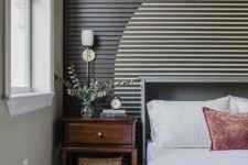an eye-catching wood slat accent wall with a painted circle, a grey bed with bedding, a stained nightstand and some printed rugs