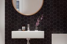 an ultra-modern powder room with black hexagon tiles, a floating sink, a white toilet and a round mirror – nothing else is needed