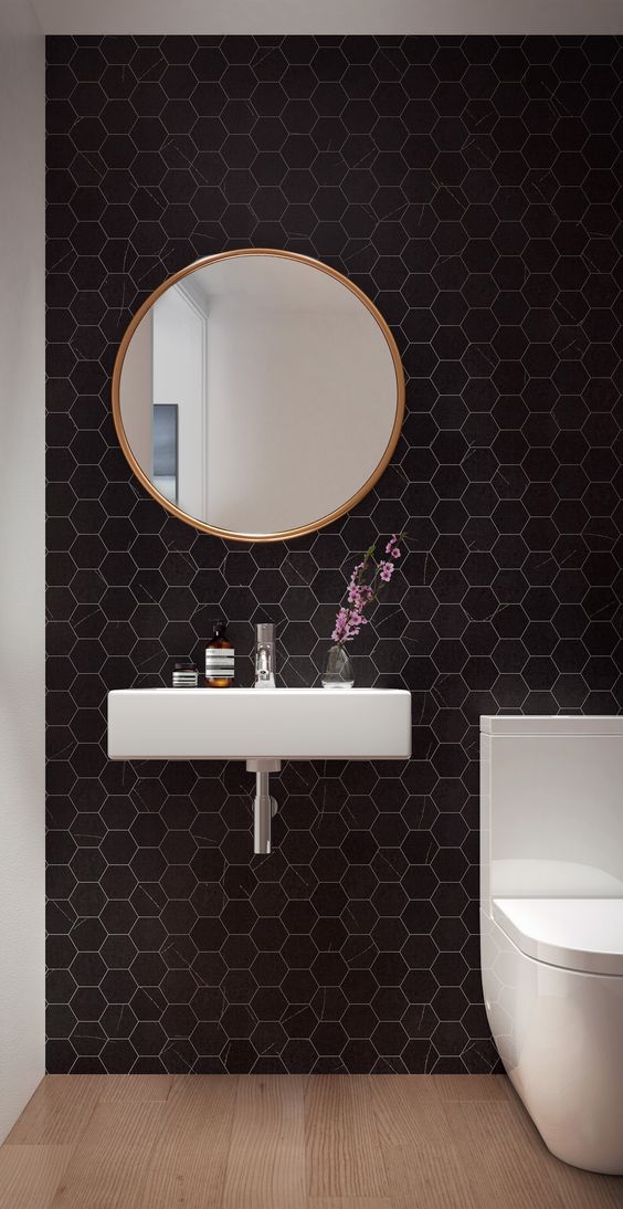 An ultra modern powder room with black hexagon tiles, a floating sink, a white toilet and a round mirror   nothing else is needed