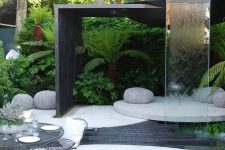 03 a contemporary outdoor space with a concrete round deck, a dining space, a round platform with pebbles and a waterfall of glass