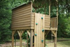 16 a light-stained wooden house with a rope ladder, a small climbing wall under the trees is a lovely idea for kids to have fun