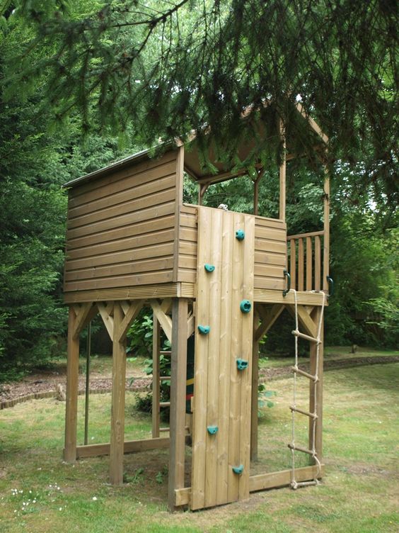 A light stained wooden house with a rope ladder, a small climbing wall under the trees is a lovely idea for kids to have fun