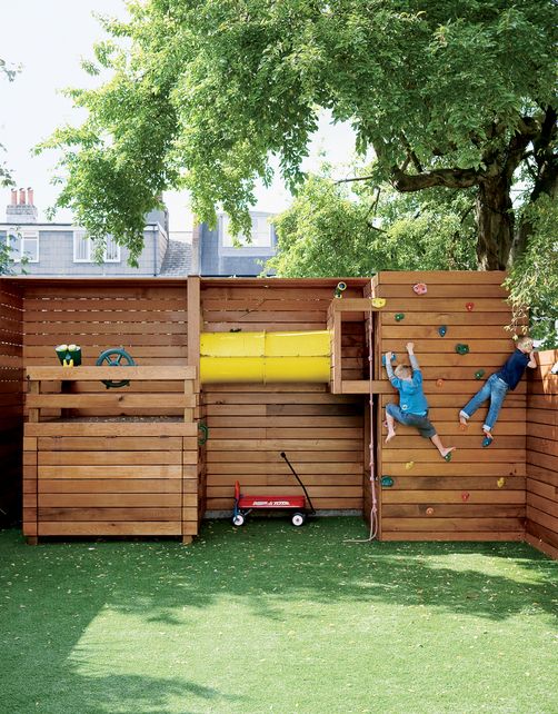 A light stained wooden playground with a climbing wall, a ship imitation and a tube for kids to play