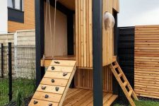 19 a modern light-stained kids’ house with a ladder and a climbing wall and a sphertic window is a lovely idea