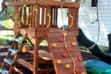 20 a small stained playhouse with a green slide, a ladder, a climbing wall, a dining set under the house is a fun and cool idea to rock