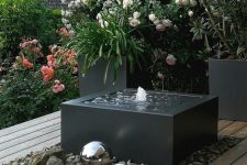 22 a modern interpretation of a fountain, with a black bow, pebbles around and some silver spheres next to it is a cool idea